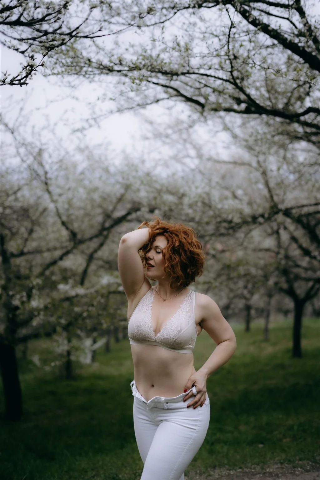 Christina among orchard trees in a white lace top
